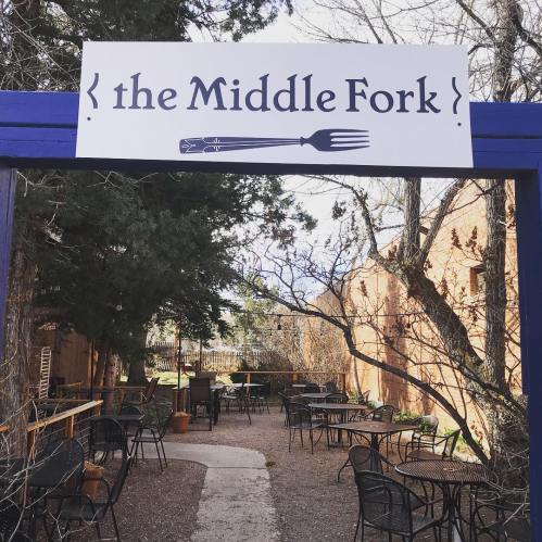 Sign for "the Middle Fork" restaurant with outdoor seating area and trees in the background.