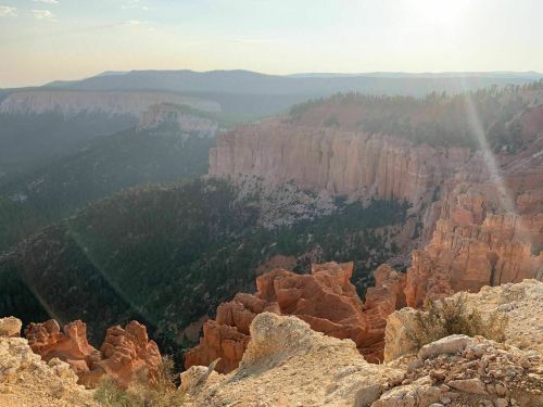 A scenic view of rugged cliffs and valleys under a hazy sky, with sunlight illuminating the landscape.