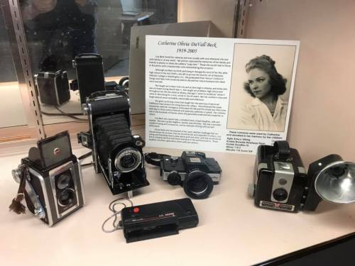 A display of vintage cameras and a plaque honoring Catherine Olivia Orval Beck, 1919-2018, with her biography.