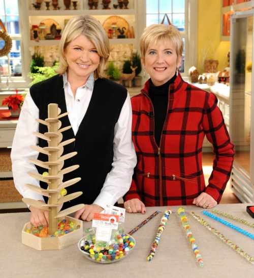 Martha Stewart and a guest stand beside a colorful craft display, featuring a wooden tree and decorated candy sticks.
