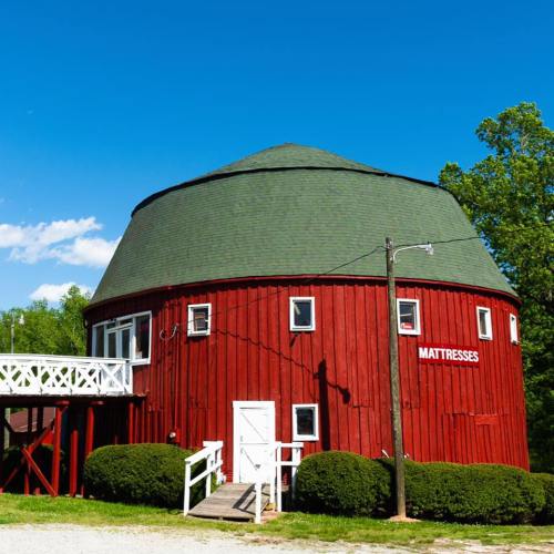 A red, round building with a green roof, featuring a sign that says "MATTRESSES" and surrounded by greenery.
