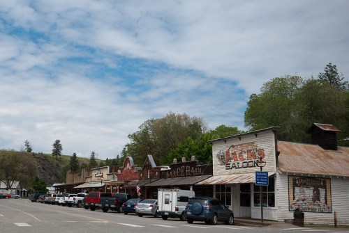 A quaint street scene featuring rustic buildings and parked cars under a cloudy sky.