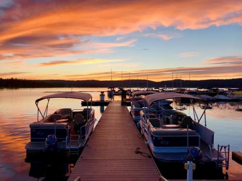 A serene sunset over a lake, with boats docked along a wooden pier and colorful clouds reflecting on the water.