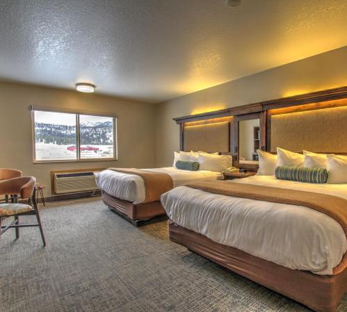 Cozy hotel room with two beds, warm lighting, and a view of snowy mountains outside the window.