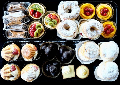 A variety of colorful pastries, including cannoli, fruit tarts, donuts, and cream-filled treats, arranged on a tray.