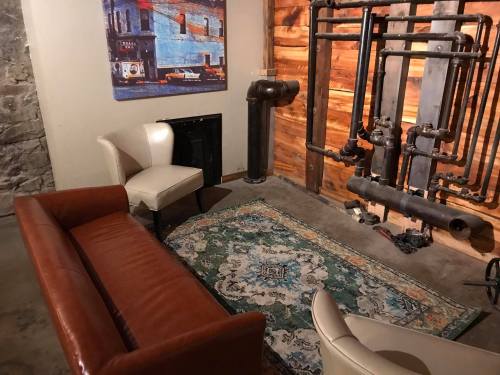 Cozy room with a brown sofa, white chairs, a patterned rug, and exposed pipes against a wooden wall.