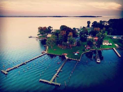 Aerial view of a serene island with docks, lush greenery, and houses by the water at sunset.