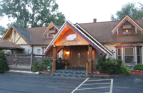 A charming restaurant with a wooden exterior, "OPEN" sign, and festive decorations, surrounded by greenery.