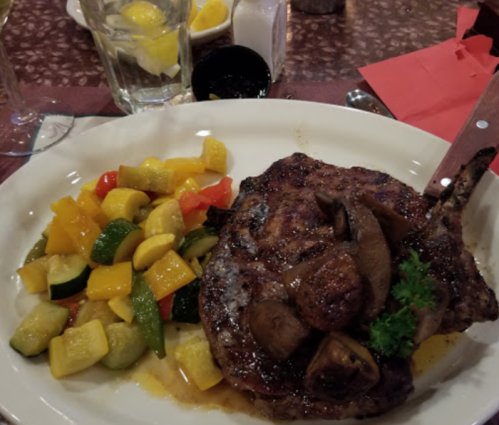 A grilled pork chop topped with mushrooms, served with a side of sautéed vegetables including zucchini and bell peppers.