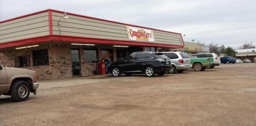 A storefront with a red and beige exterior, featuring parked cars in front and a cloudy sky above.