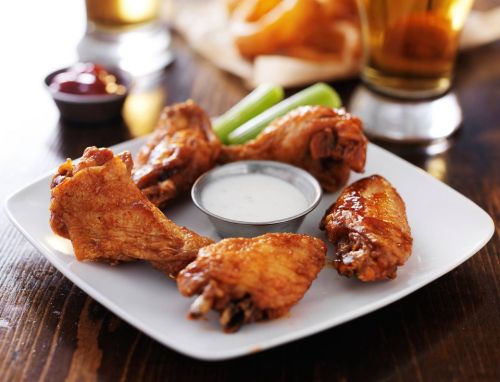 A plate of crispy chicken wings with a side of ranch dressing, celery sticks, and dipping sauces.