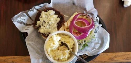 A plate with a burger topped with cheese, a side of coleslaw, and a bowl of mashed potatoes.