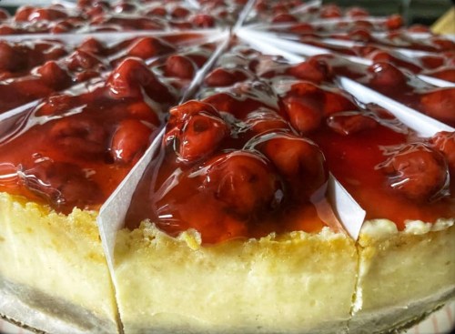 A close-up of a cheesecake topped with glossy red cherry glaze and sliced into wedges.