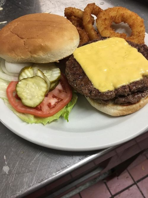 A cheeseburger with lettuce, tomato, pickles, and onion on a plate, accompanied by onion rings.