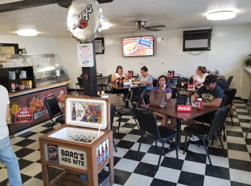 A casual dining area with tables, customers enjoying food, and a counter displaying menu items and drinks.