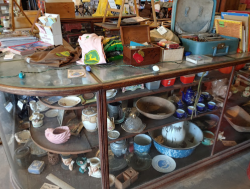 A vintage display case filled with various antiques, including dishes, trinkets, and clothing items.