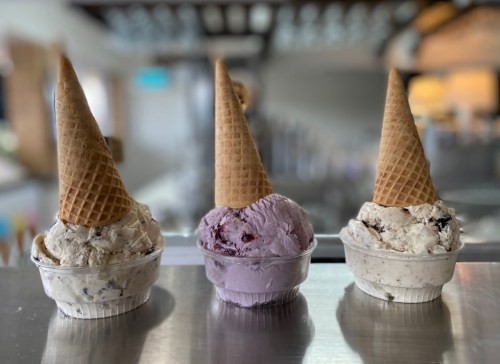 Three ice cream cones with different flavors sit in cups on a counter, showcasing a variety of textures and colors.