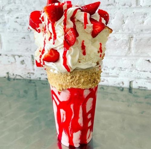 A tall milkshake topped with whipped cream, fresh strawberries, and a drizzle of strawberry sauce, served in a glass.