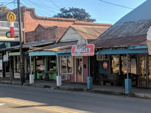 A quaint street scene featuring shops, including Angelle's, with colorful signage and rustic architecture.