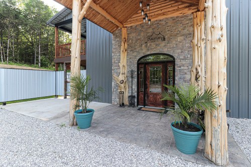 Entrance of a rustic stone building with wooden accents, featuring potted plants and a gravel pathway.