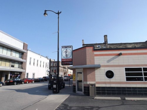 A street view of Kewpee Hamburgers with a retro sign, showcasing an open status and nearby buildings.