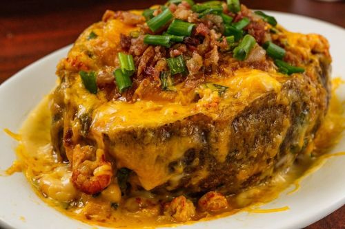 A cheesy, baked dish topped with green onions and bacon, featuring seafood and a creamy sauce, served on a white plate.