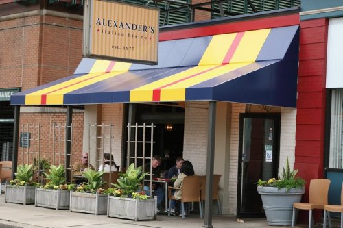Exterior of Alexander's Italian Bistro with colorful awning, outdoor seating, and planters. Established 1977.