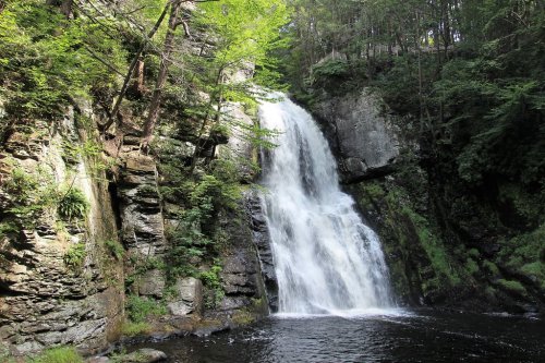 A serene waterfall cascading down rocky cliffs, surrounded by lush green trees and a calm pool at the base.
