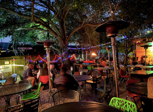 A cozy outdoor dining area with colorful lights, heaters, and people enjoying the evening atmosphere.