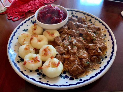 A plate of beef stew with dumplings and a side of cranberry sauce, garnished with herbs and bacon bits.