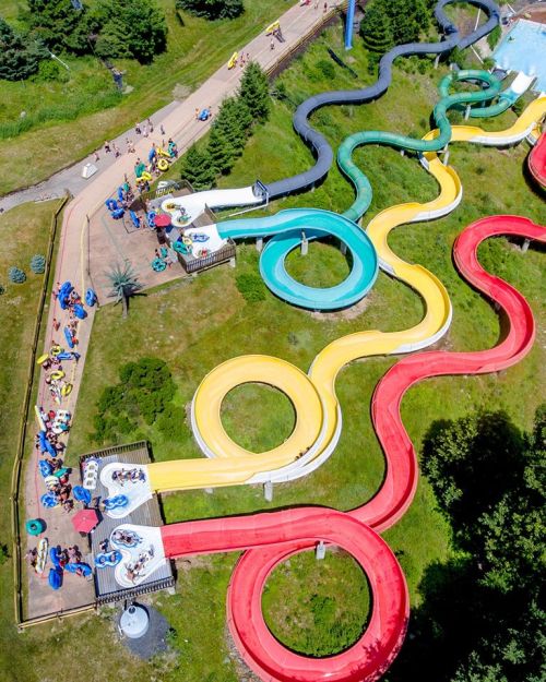 Aerial view of colorful water slides winding through a grassy area, with people enjoying the park below.