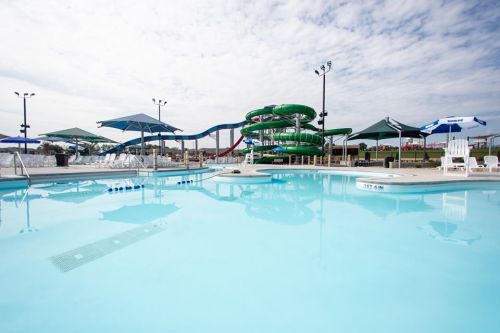 A clear blue pool with lounge chairs and umbrellas, featuring a large green water slide in the background.