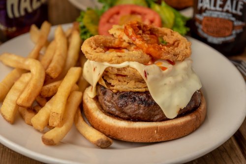 A juicy burger topped with melted cheese, crispy onion rings, and served with fries and fresh tomato on a plate.