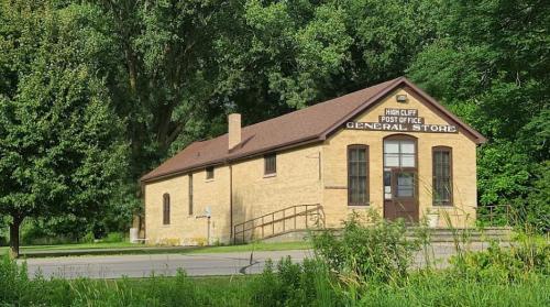 A brick building with a sloped roof, labeled "High Cliff Post Office General Store," surrounded by trees.
