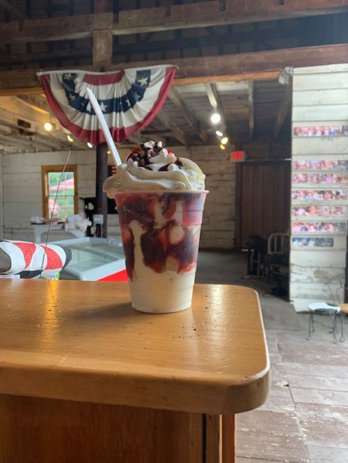 A delicious sundae in a cup topped with whipped cream, chocolate syrup, and a cherry, set on a wooden counter.