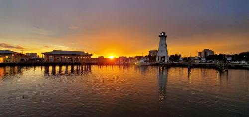 A serene sunset over a harbor, featuring a lighthouse and reflections on the water.