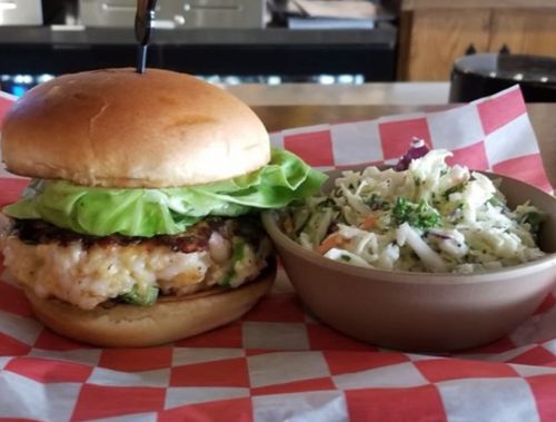 A crispy chicken sandwich with lettuce on a bun, served with a side of coleslaw in a bowl.