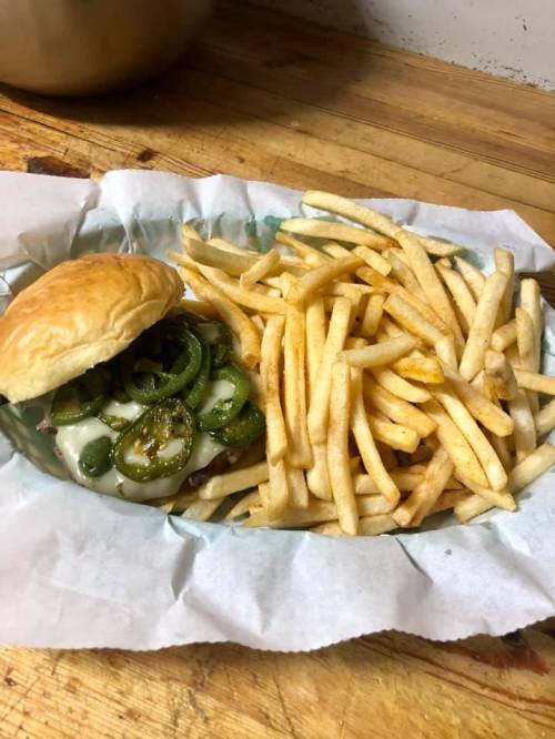 A sandwich with jalapeños and melted cheese beside a serving of golden French fries on a wooden surface.