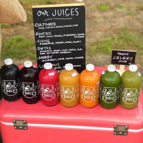A display of colorful juice bottles in front of a chalkboard menu listing various juice flavors.