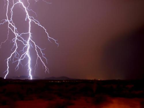 A dramatic lightning strike illuminates a dark sky over distant mountains during a storm.