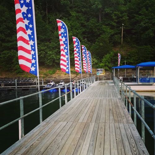 A wooden dock lined with American flag banners, surrounded by greenery and water.