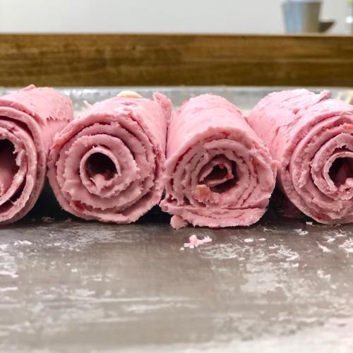 Four pink ice cream rolls neatly arranged on a metal surface, with a smooth texture and swirls visible.