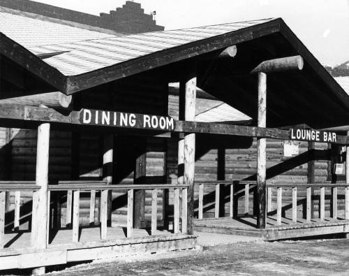 Black and white photo of a wooden building with signs for "Dining Room" and "Lounge Bar" on the porch.