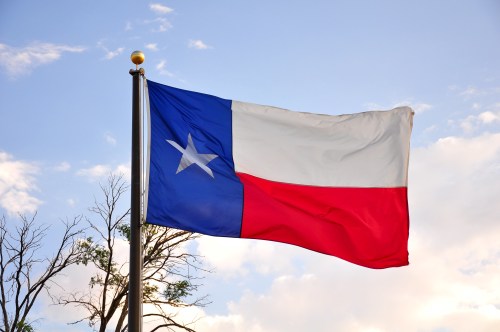 Texas state flag waving against a blue sky with clouds.