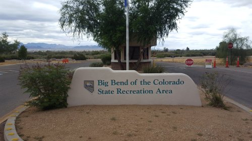 Sign for Big Bend of the Colorado State Recreation Area, with a desert landscape and cloudy sky in the background.