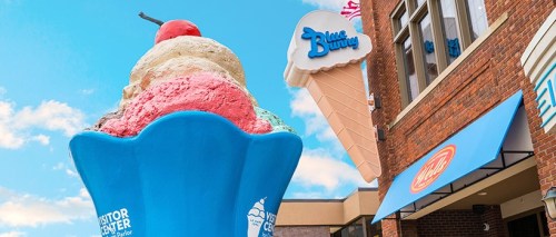 A large ice cream cone sculpture in front of a building with a Blue Bunny sign and a clear blue sky.