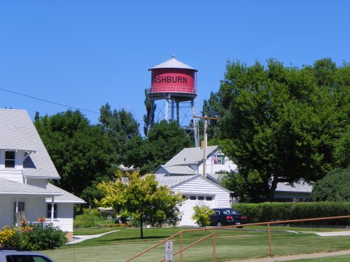 A red water tower labeled "ASHBURN" stands among green trees and houses under a clear blue sky.