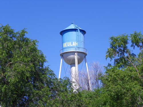 A blue water tower labeled "BEULAH" stands tall among green trees against a clear blue sky.