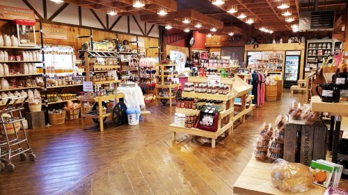 A cozy store interior filled with wooden shelves, jars of preserves, and various local products, with warm lighting.
