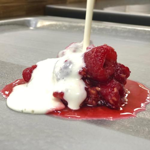 Fresh raspberries topped with a drizzle of cream, creating a vibrant red and white dessert on a gray surface.